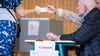 Eine Wahlhelferin gibt einen Stimmzettel aus. Landesweit fällt die Wahlbeteiligung unterschiedlich aus.