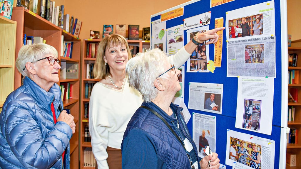 Bibliothekschefin Bärbel Dänecke zeigt den Besucherinnen Hanna Klietz und Giesela Cherek am Tag der offenen Tür die Ausstellung zum 33-jährigen Bestehen der Bibliothek auf der Wasserburg.