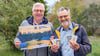 Roland Schwarz und Horst Naumann präsentieren den Adventskalender 2025 der Lions und die beiden Hauptgewinne in Form von je zwei Goldplättchen. 