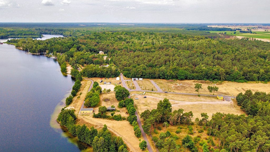 Blick auf das nördliche Ufer des Bergwitzsees: Auf der Wiese im Vordergrund plant Resort-Chef Marek Staginnus den Ausbau mit zusätzlichen Reisemobil-Stellplätzen, Mobilheimen und später einer neuen Gastronomie.
