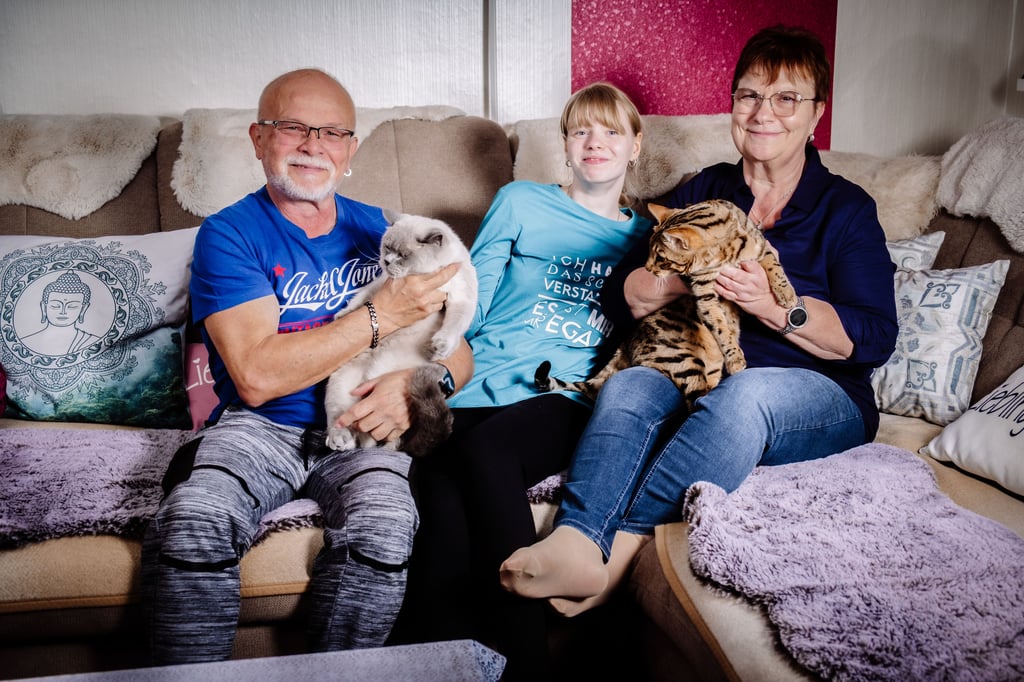 Pflege mit Herz: Gabriele und Tino Kopf mit ihrer Pflegetochter Luisa und den Familienkatzen auf dem Sofa.