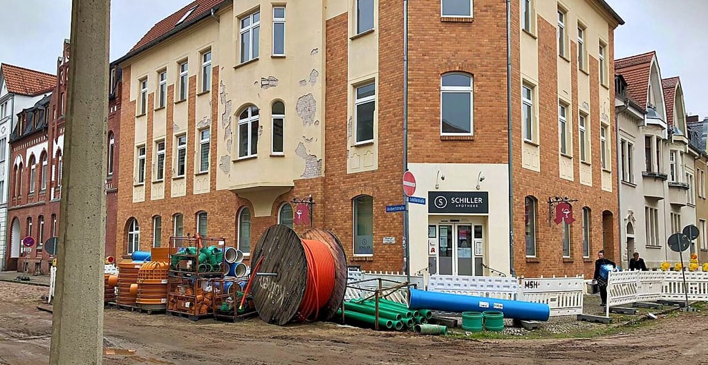 Blick von der Baustelle auf die Schiller-Apotheke an der Ecke Schiller-/Aribertstraße: Links neben der Apotheke, im Haus Aribertstraße 34, befinden sich Praxen von Hausärzten und Gynäkologen sowie die Praxis eines Internisten.
