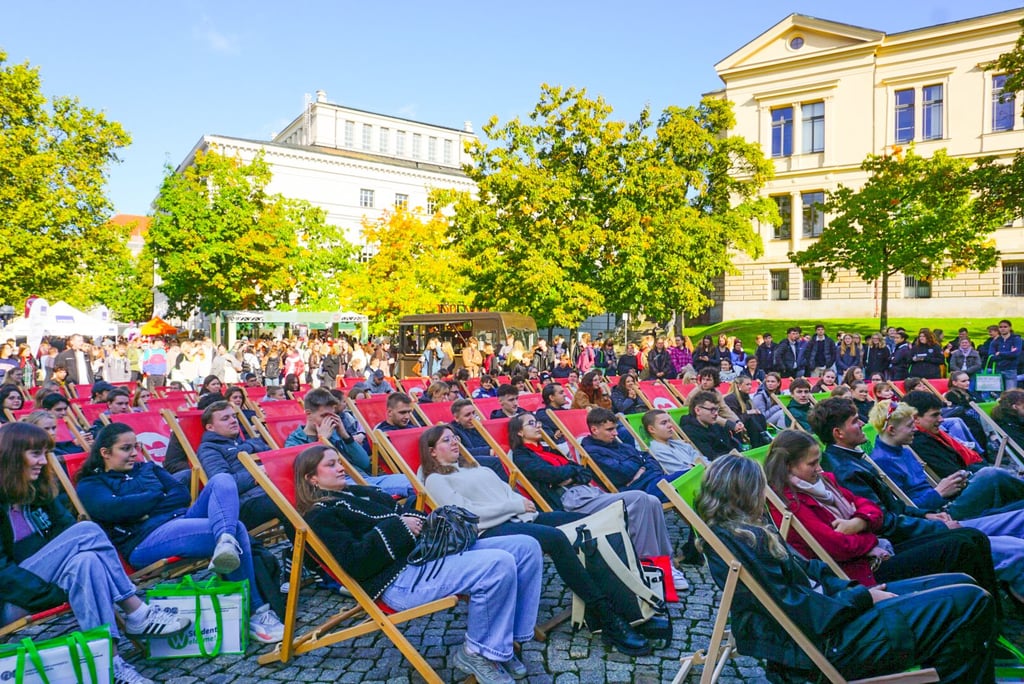Dem Bühnenprogramm zur feierlichen Immatrikulation auf dem Uniplatz können Studierende im Liegestuhl zusehen.