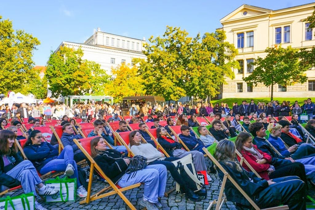 Dem Bühnenprogramm zur feierlichen Immatrikulation auf dem Uniplatz können Studierende im Liegestuhl zusehen. 