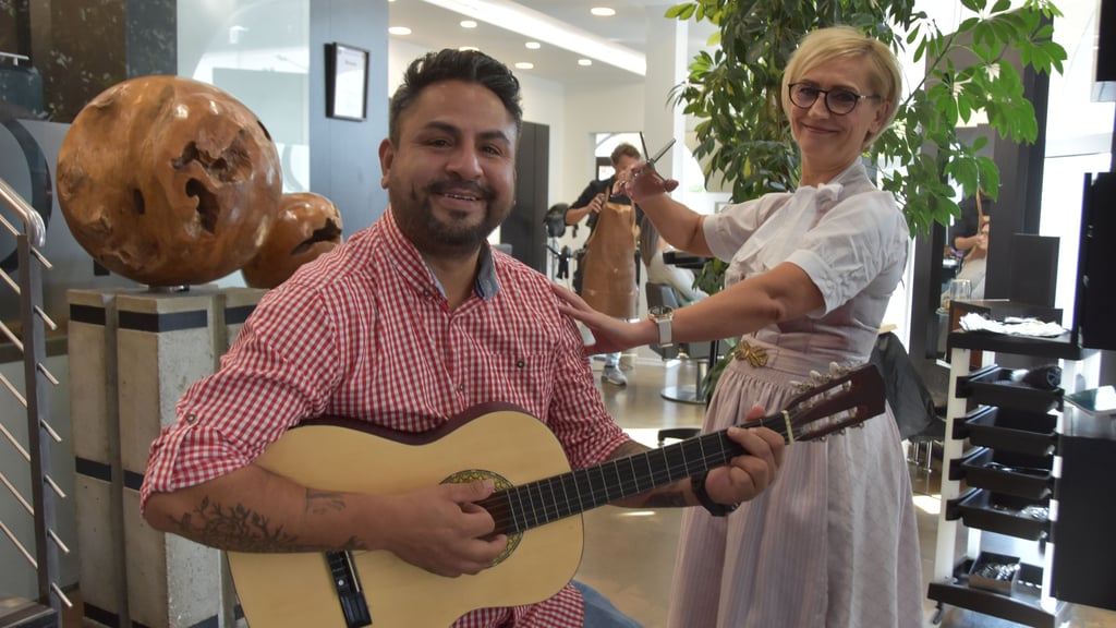 Gilberto Sánchez spielt auf der Gitarre und singt dazu. Der Kathendorfer bringt musikalisches Flair in den Wolfsburger Salon „IT'S//IN Meisterfriseure“, während seine Kollegin Ella Geist mit der Schere zaubert – echte Leidenschaft im Oktoberfest-Outfit.