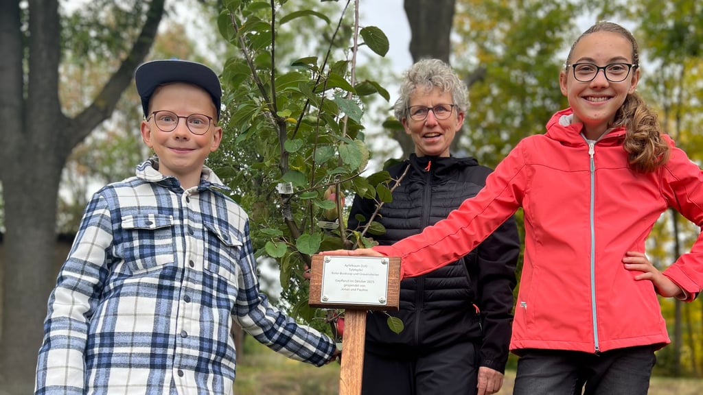 Jonas und Pauline, mit Ilka Linkohr im Hintergrund, an ihrem gepflanzten Baum.