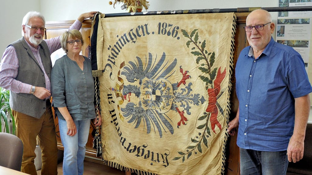 Bürgermeister Uwe Lenz (links) und das Späninger Ehepaar Karin und Gerhard Jung präsentieren mit der Traditionsfahne des Kriegervereins von 1876 ein Stück Späninger Dorfgeschichte, das für 1.300 Euro den Besitzer wechselte.