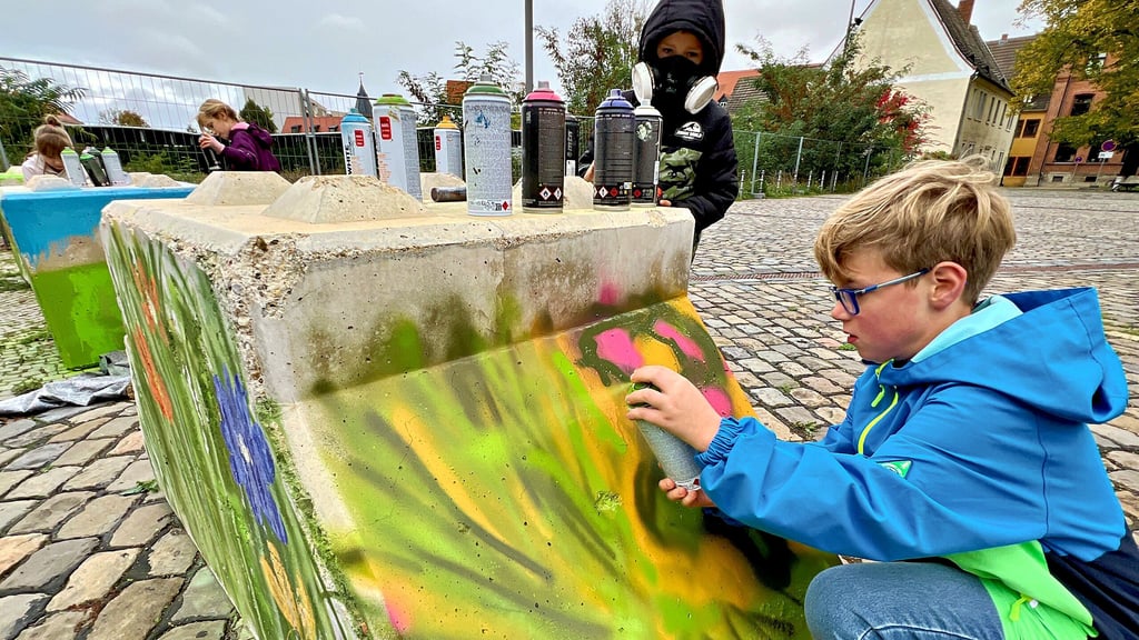 Die Zweitklässler Erwin (vorn rechts) und Luan gestalten gemeinsam einen der Poller vor der Bernburger Marienkirche.