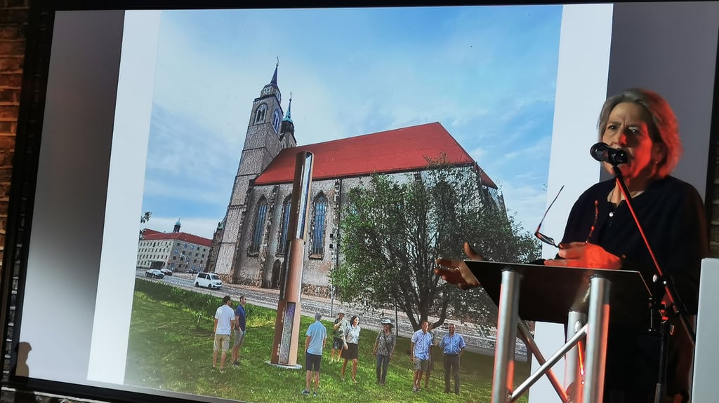 Künstlerin Maria J. Fernández entwarf eine Säule. Sie greift das Konzept der zwölf Epochen Magdeburgs auf, die in einer dynamischen Bewegung um die Säule angeordnet sind – wie eine Spirale durch die Zeit.