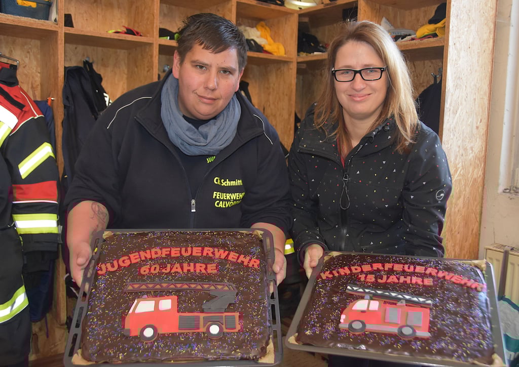 Katharina Kehler (rechts) überreicht zwei große Bleche voller Kuchen samt süßer Deko an Christine Schmittke. Tommy, der Sohn von Katharina Kehler, gehört zur Kinderfeuerwehr.