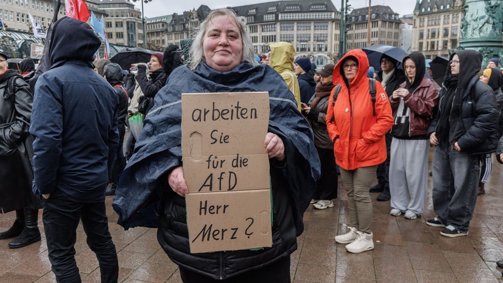 Eine Demonstrantin in Hamburg stellt auf einem Pappschild eine Frage an Bundeskanzler Friedrich Merz (CDU).
