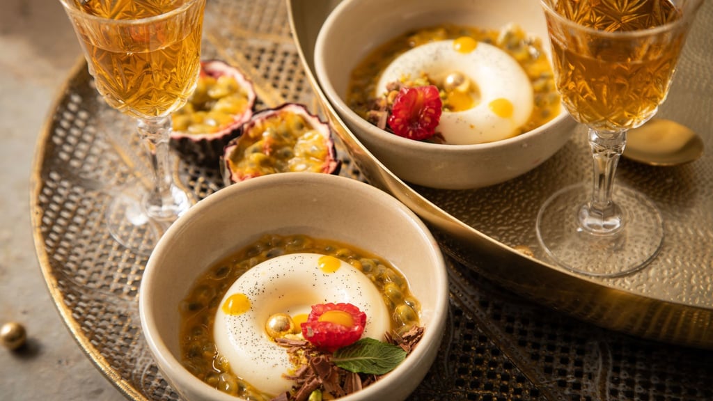 Panna Cotta mit Passionsfrucht, Himbeere, Mangotupfer, Minze, Pistazie, Schokolade und goldenen Schokokugeln in Savarin-Form zubereitet. Das ist eine Backform in flacher, ringförmiger Gestalt.