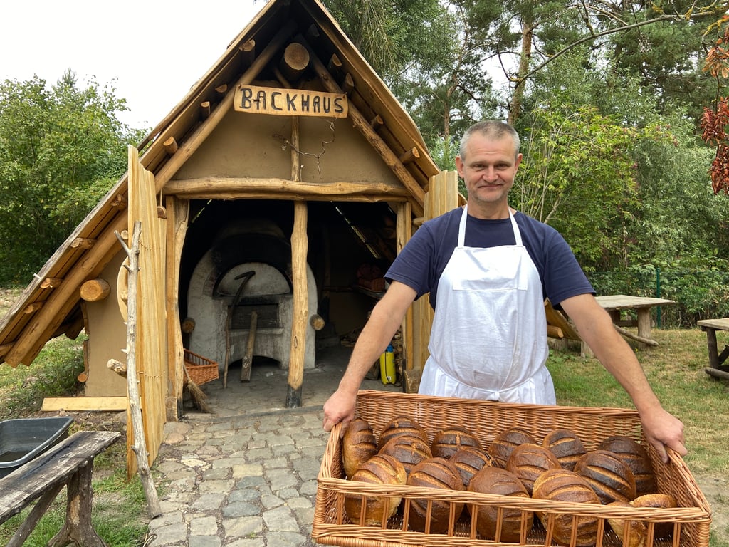 Frisch aus dem Lehmofen: Mike Amthor präsentiert einen Korb mit duftenden Broten vor der selbstgebauten Backhütte im Steinzeitdorf Randau – gebacken wie vor hunderten Jahren, ganz ohne Strom und Technik.