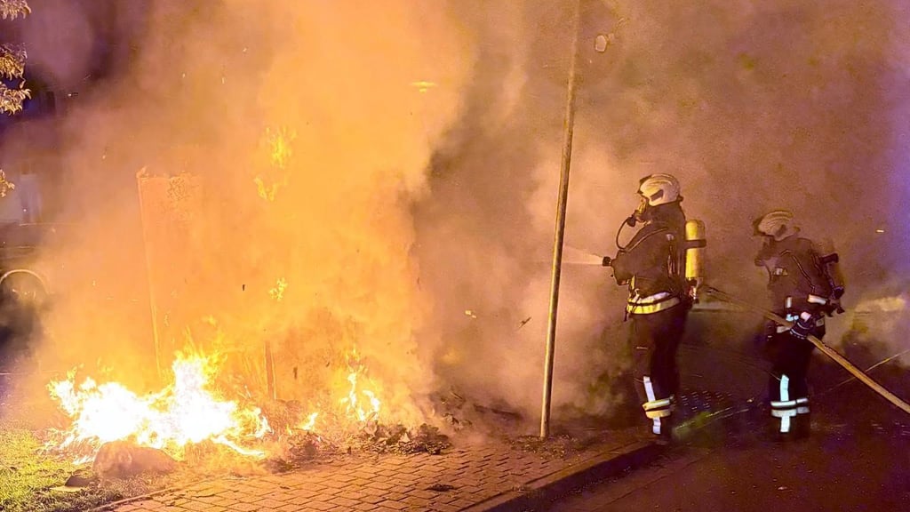 Mit Atemschutz und C-Rohr sind die Feuerwehrleute in Haldensleben an der Schulstraße im Einsatz: Die Container werden geöffnet, der Inhalt auseinandergezogen und sorgfältig abgelöscht.