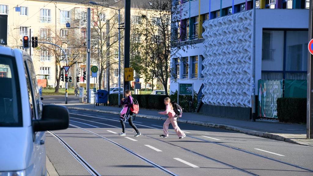 Schüler in Magdeburg hasten in einer Lücke im Autoverkehr über die Straße vor ihrer Schule.