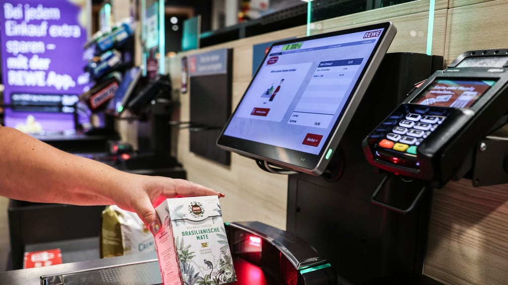 Eine Frau scannt in einer Rewe-Filiale eine Packung Teebeutel an einer Selbstbedienungskasse.