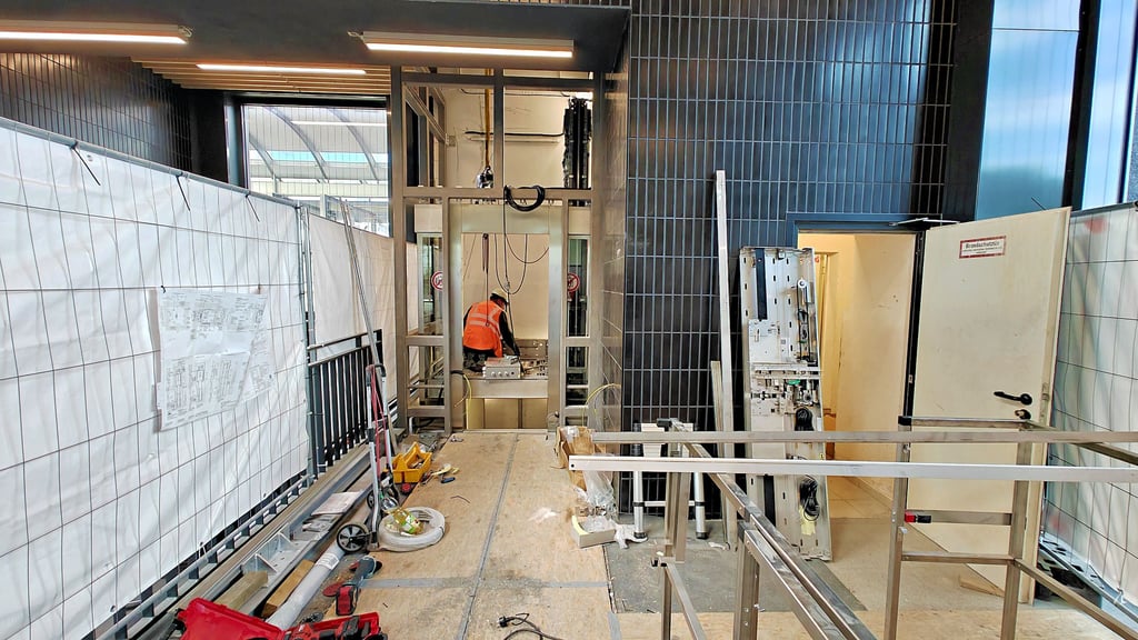 Hinter dem Bauzaun an der Treppe zur Unterführung wird ein neuer  Aufzug montiert. Die Hydrauliktechnik wird durch Seilaufzüge ersetzt. 