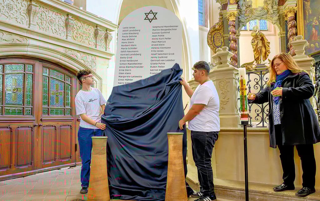 Zwei Schüler der „Hus“-Schule enthüllen  die Gedenktafel mit den Namen der ermordeten  und  vertriebenen Naumburger Juden.  Pfarrerin Christina Lang führt durch die Veranstaltung und zündet eine Kerze an.  