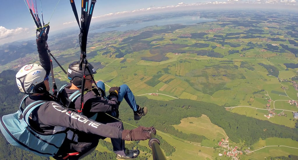 Flug über die grüne Landschaft Bayers mit dem Paraglider: Im Hintergrund ist der Chiemsee zu sehen. 