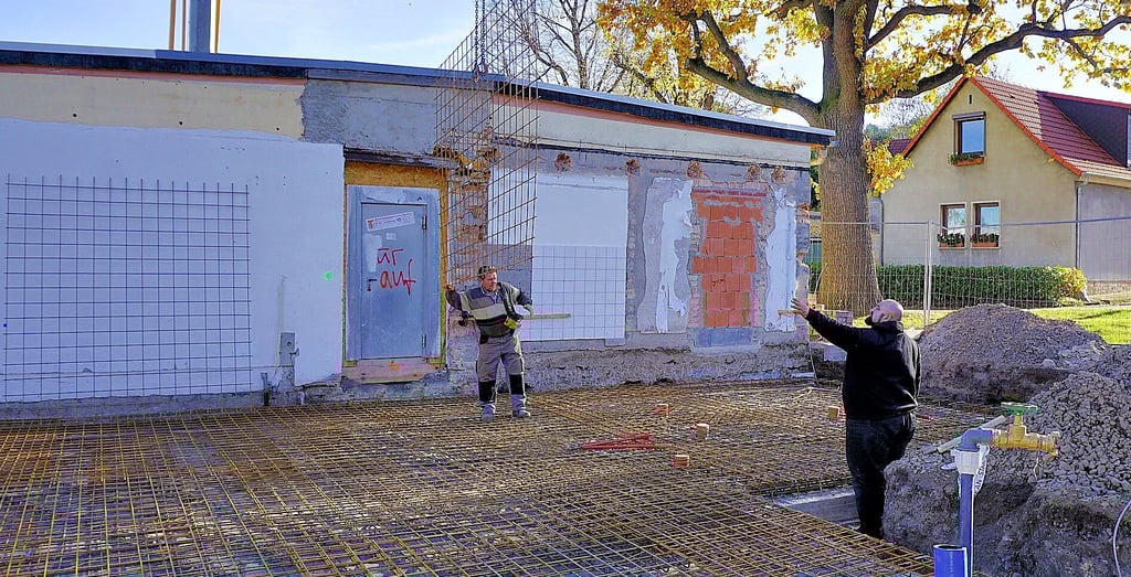 Volker Burghardt von der bauausführenden Firma (links) verlegt mit einem Kollegen Eisengitter für die Bodenplatte. 
