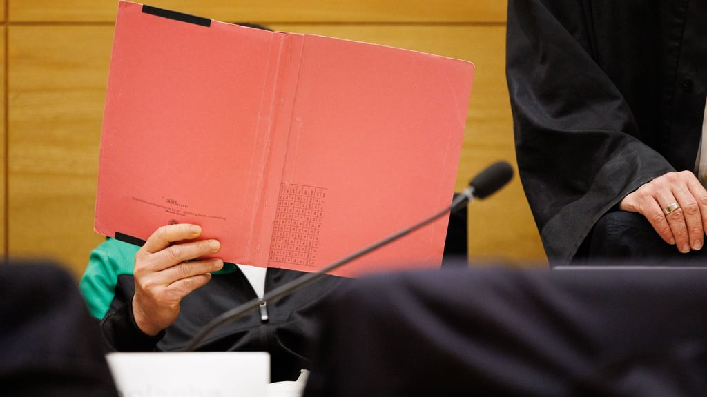 Einer der Angeklagten am Landgericht Bielefeld sitzt neben seinem Verteidiger und verdeckt sein Gesicht.