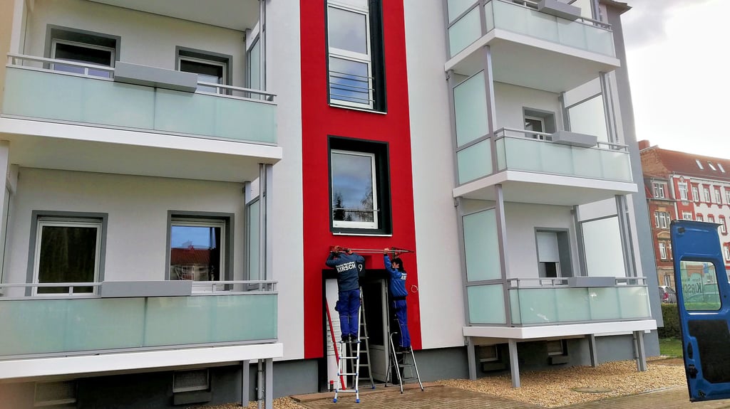 Die Fassade frisch gedämmt und eine neue Balkonanlage – so zeigt sich der Block in der Aylsdorfer Straße.  Handwerker montieren ein Vordach.   