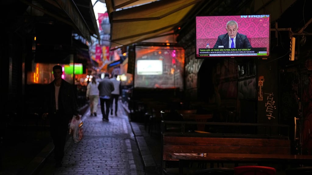 Menschen gehen an einem Fernsehbildschirm vorbei, auf dem der Präsident des Türkischen Fußballverbands, Ibrahim Haciosmanoglu, während einer Pressekonferenz zu sehen ist.