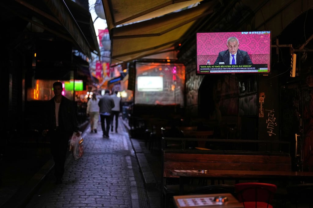 Menschen gehen an einem Fernsehbildschirm vorbei, auf dem der Präsident des Türkischen Fußballverbands, Ibrahim Haciosmanoglu, während einer Pressekonferenz zu sehen ist.