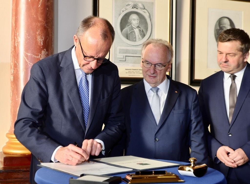 Friedrich Merz (links) trägt sich ins Gästebuch der Landesregierung und der Leopoldina ein.