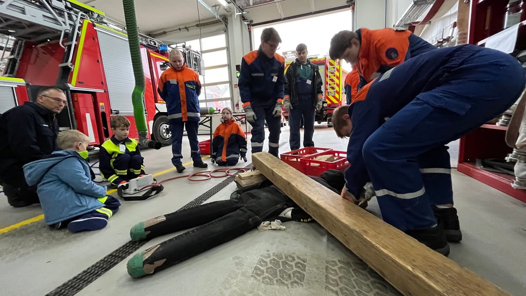 Gemeinsam üben Mädchen und Jungen unter Anleitung erfahrener Feuerwehrmänner den Einsatz von hydraulischen Geräten, um die eingeklemmte Puppe befreien zu können.