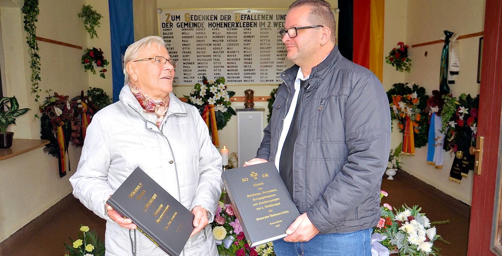 Raimo Bunde und die Heimatvereinsvorsitzende Ursula Pennigsdorf  mit den Gefallenenchroniken vorm Mahnmal in Hohenerxleben.