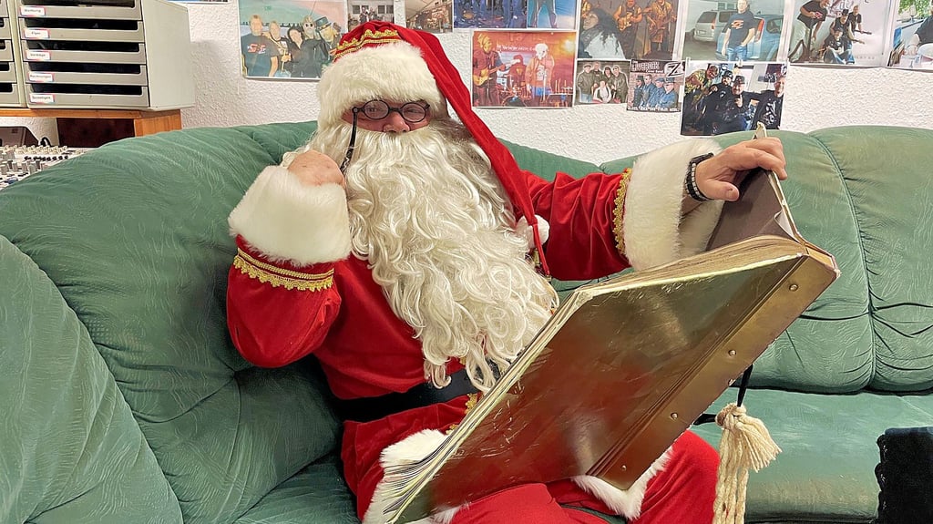 Steffen Seitz sitzt im Probenraum seiner Band „Fazit“ in Weißenfels und trägt das Weihnachtsmannkostüm samt Brille und goldenem Buch. 