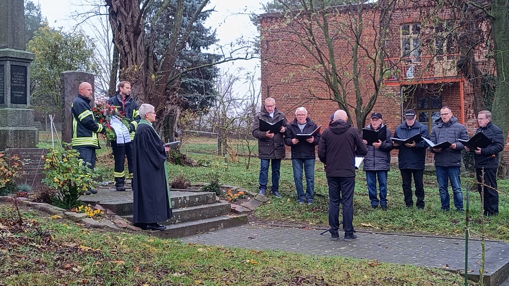 Gemeinsames Gedenken am Ehrenmal. Die Pastorin Esther Spenn lauscht mit Vertretern der freiwilligen Feuerwehr dem Hödinger Männerchor.
