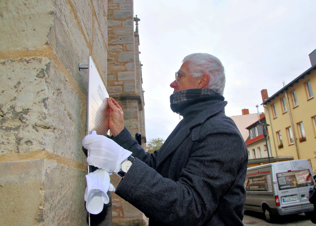 Der Hallenser Künstler Thomas Leu schraubt hier die Erklärtafel zu der Schmähplastik an die Kirchenwand.