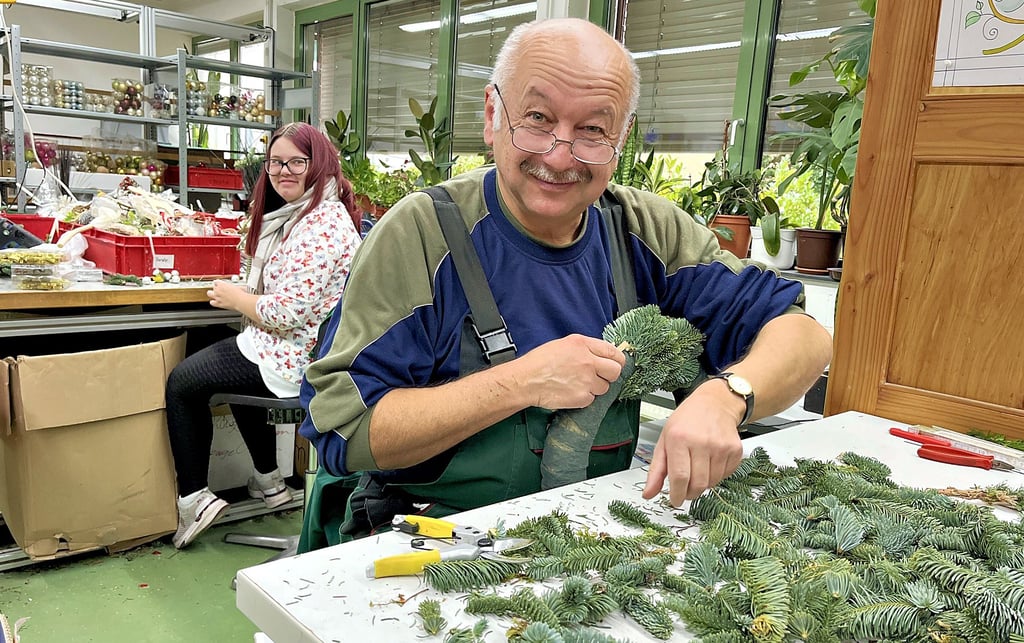 In der Floristikwerkstatt der Lebenshilfe in Tangerhütte werden ganz frisch die Kränze aus Tannengrün gewickelt. Dirk Richter (vorn) macht das seit 26 Jahren und hat immer noch Spaß an allem, was  die Weihnachtszeit verschönert. Kollegin Tabea Feindt im Hintergrund ist eine der Jüngeren in der Werkstatt. 