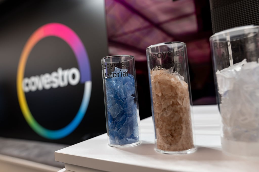 Eine deutsche Firma wird arabisch: Das Logo des Spezialchemie-Konzerns in einem Firmen-Showroom, davor Gläser mit Covestro-Materialien.