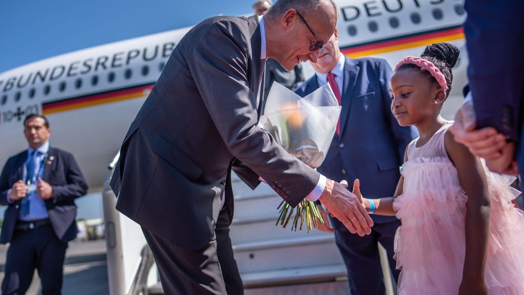 Kanzler Friedrich Merz wird auf dem Flughafen von Johannesburg von einem Mädchen begrüßt.