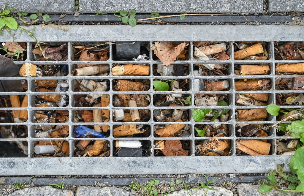 Zigarettenkippen in einem Abflussgitter für Regenwasser.