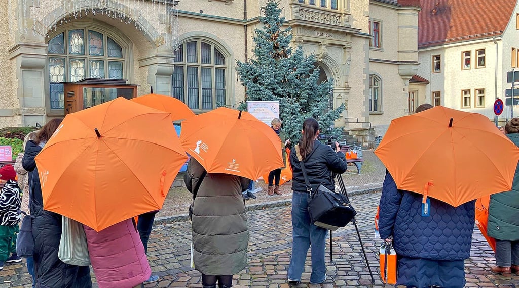 Orange farbene Schirme leuchten während der Worte von Silvia Ristow vor dem Rathaus.