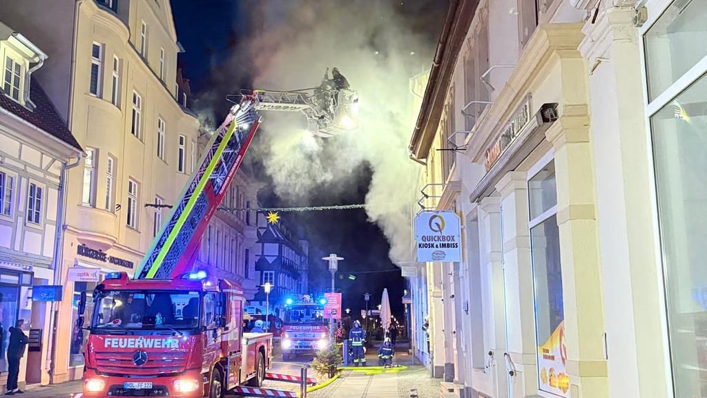 Die Feuerwehr rückt mit Drehleiter und mehreren Fahrzeugen an, während dichter Rauch aus dem Dachbereich eines Geschäftshauses in der Hagenstraße aufsteigt.
