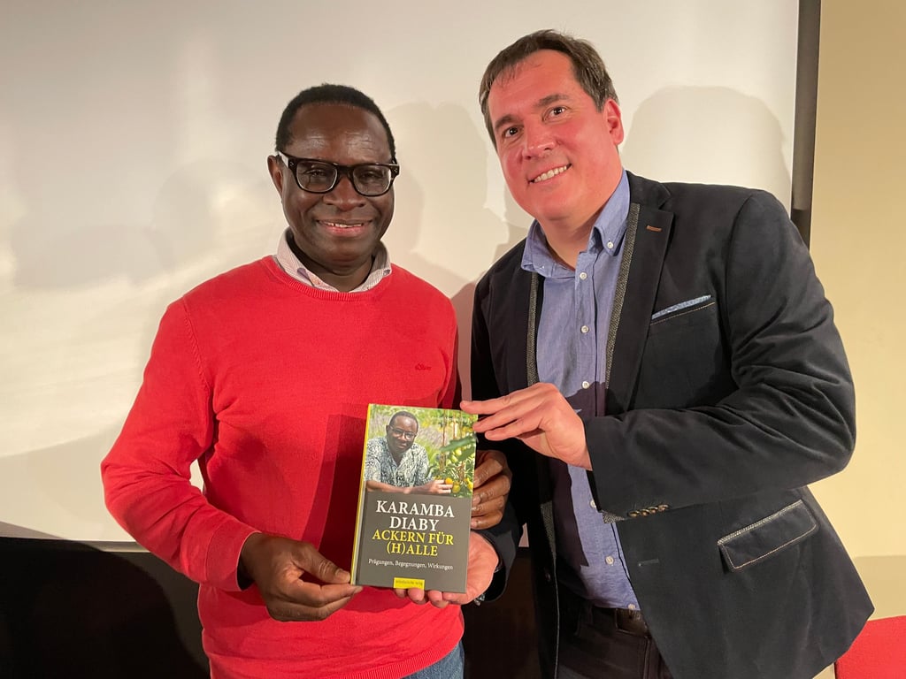 Überraschung gelungen: Karamba Diaby, von 2013 bis 2025 für die SPD im Bundestag (l.), und Andrej Stephan, stellvertretender SPD-Stadtvorsitzender und Diabys ehemaliger Büroleiter, präsentieren das eigens für Diaby herausgegebene Buch. 