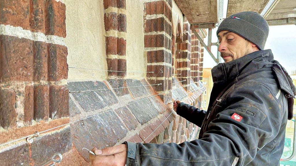 Michel Allenstein von der Dachdeckerfirma Jäger aus Kalbe (Milde) montiert in knapp 20 Metern Höhe Stahlseile an einem Sims unter den Dachzinnen der Marienkirche in Stendal.
