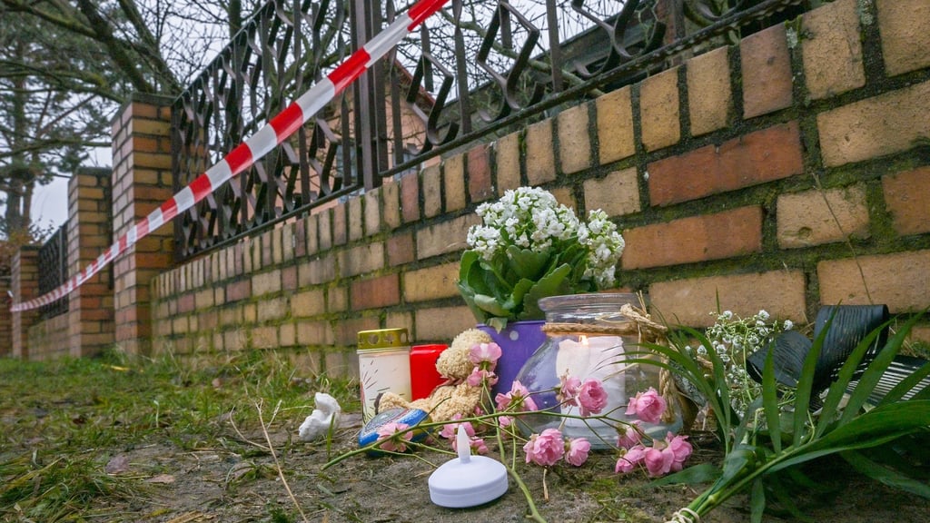 Kerzen und Blumen liegen vor einem Haus in Berlin-Mahlsdorf, in dem nach einem Feuer ein Kind gestorben ist.