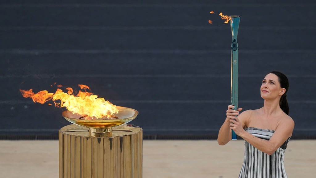 Schauspielerin Mary Mina, in der Rolle der Hohepriesterin, entzündet eine Fackel bei der Zeremonie zur Übergabe der Flamme der Olympischen Winterspiele 2026 im Panathinaikon-Stadion.