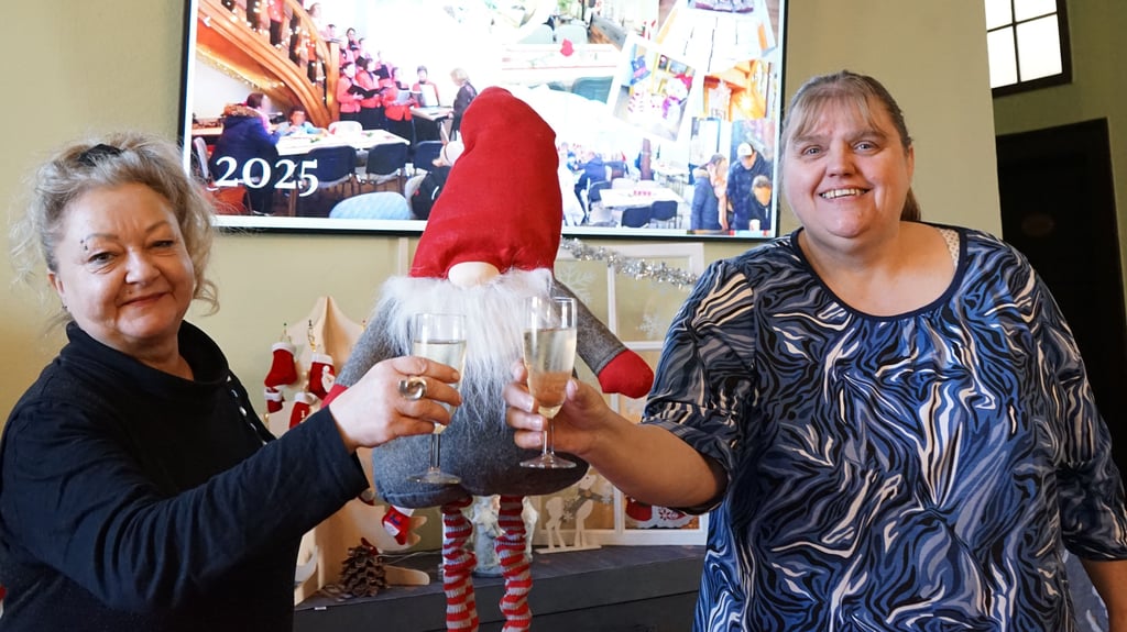 Daniela Wirthgen und Simone Becker vom Bürgerhausverein stoßen auf den neuen Bildschirm an, der im Wartebereich auf die Aktivitäten im Bürgerhaus aufmerksam macht.