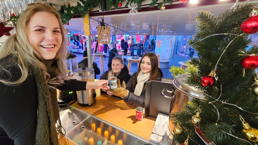 Amy  reicht den beiden Studentinnen Elly und Emelie ihren Glühwein (v.l.). 