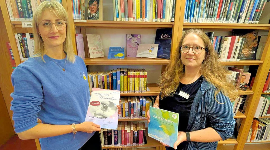 Veronika Olejnicki (l.) vom Verein Sternenkinder Dessau und Susanne Ackermann, Leiterin der Stadtbibliothek, stehen vor dem neu eingeräumten Regal. 