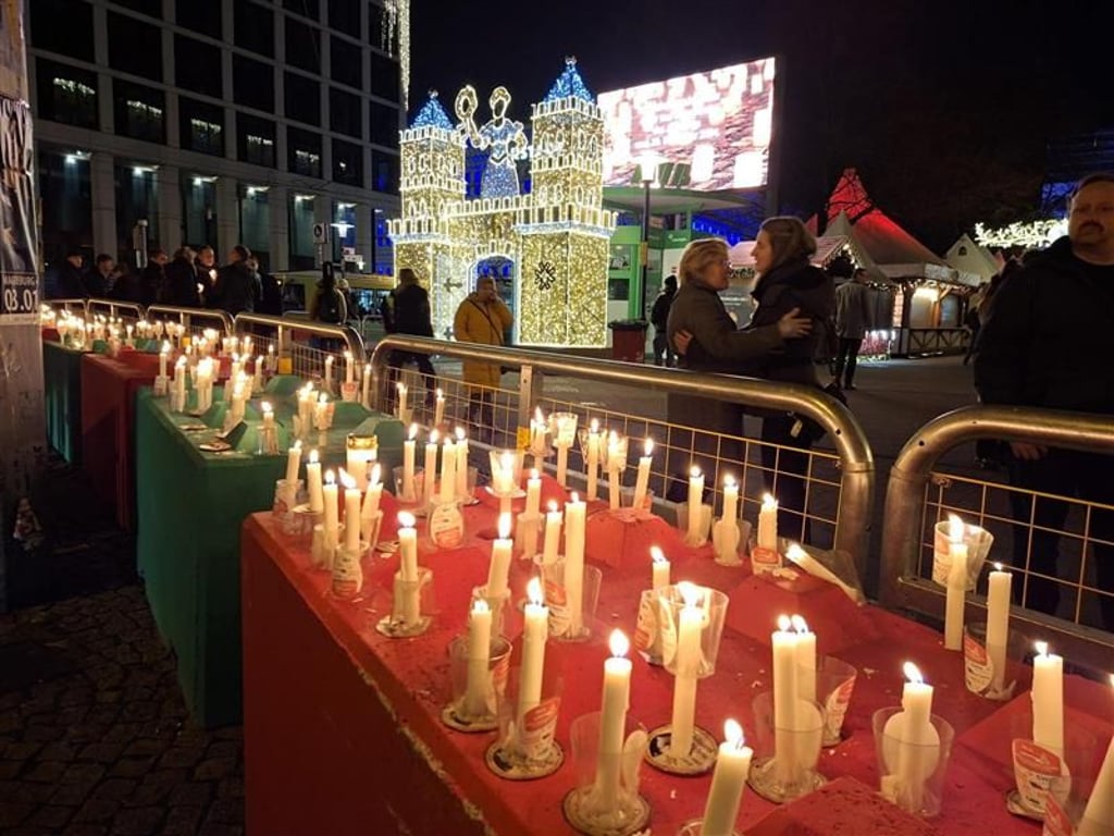 Menschen haben am Weihnachtsmarkt in Magdeburg ihre Kerzen abgestellt und trösten sich gegenseitig.