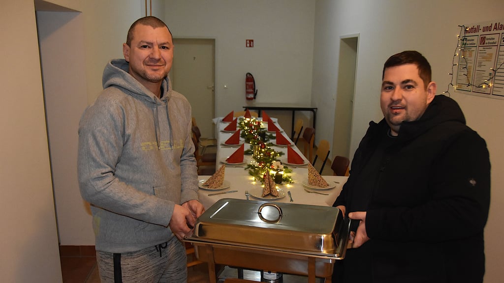Bewohner Peter Freyhold (l.) und TV-Koch Sascha Oldenburg tragen den Behälter mit dem Weihnachtsessen ins Haldensleber Obdachlosenheim. Der lange Tisch ist bereits festlich gedeckt.