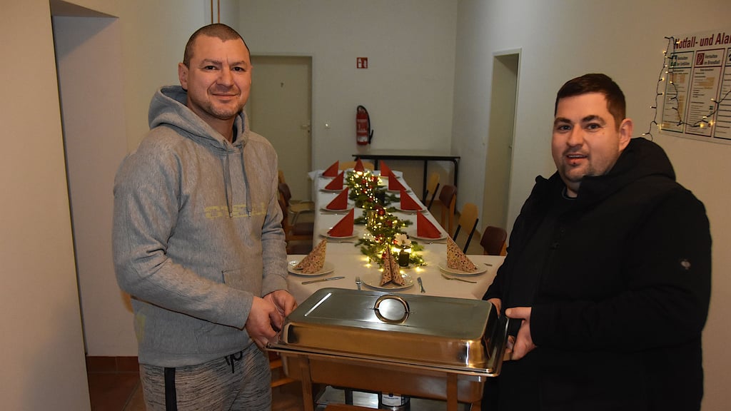 Bewohner Peter Freyhold (l.) und TV-Koch Sascha Oldenburg tragen den Behälter mit dem Weihnachtsessen ins Haldensleber Obdachlosenheim. Der lange Tisch ist bereits festlich gedeckt.